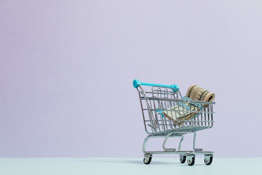 A close-up of a mini shopping cart with rolled cash on a pastel background. Ideal for finance and ecommerce themes.