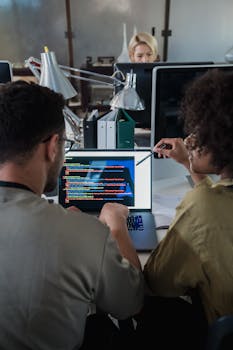 Two developers engage in software programming on a laptop in a modern office setting.