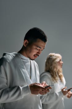 Two young adults focused on their smartphones, embodying modern technology and social connection in a studio setting.